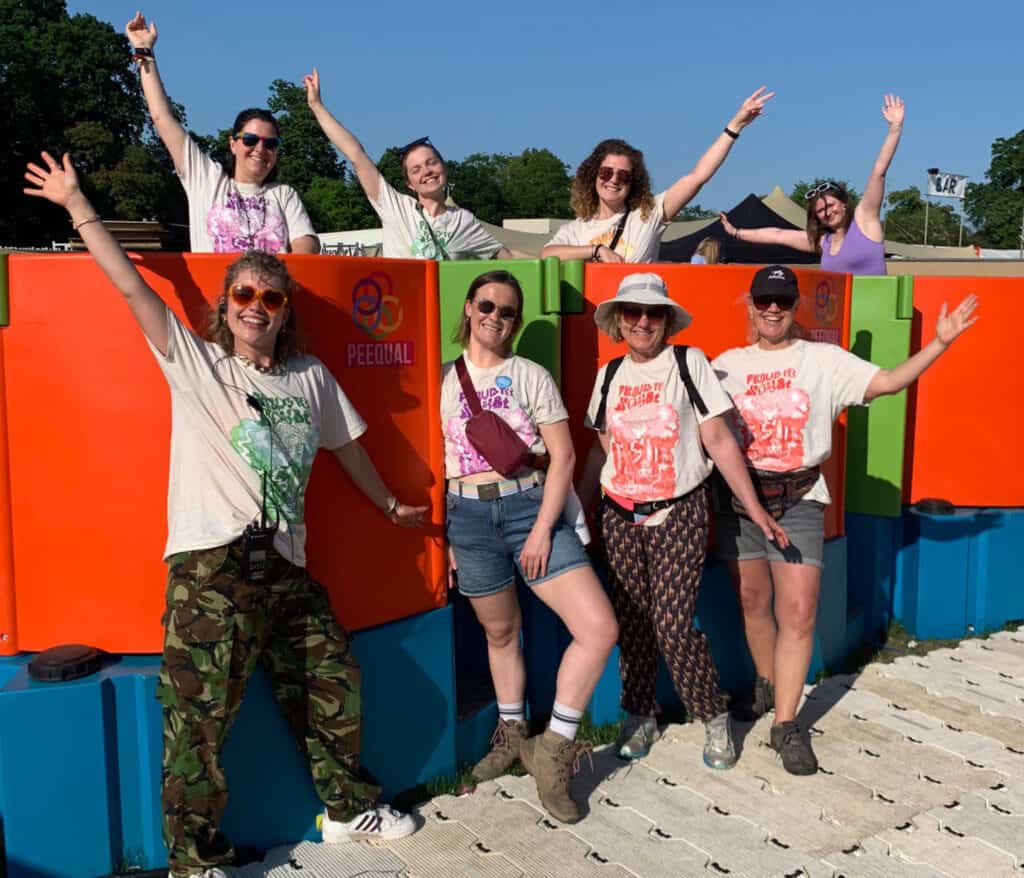 Eight women in Peequal t-shirts standing in front of a row of brightly coloured Peequal urinals.