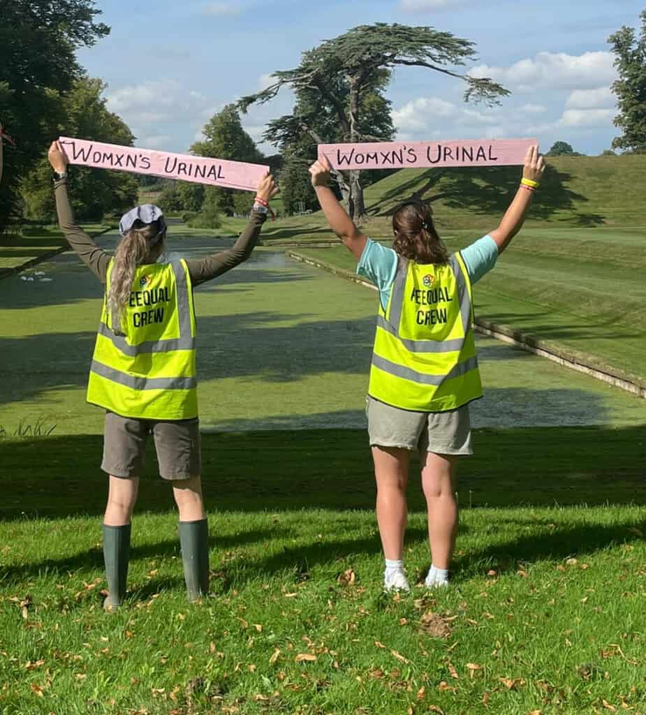 Two individuals in high-visibility vests and casual attire proudly hold up a sign reading 