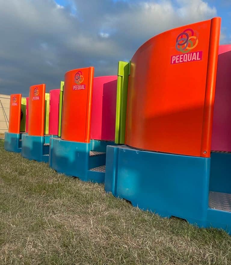A row of Peequal urinals in vibrant orange, pink, green, and blue, showcasing their innovative design for outdoor events.