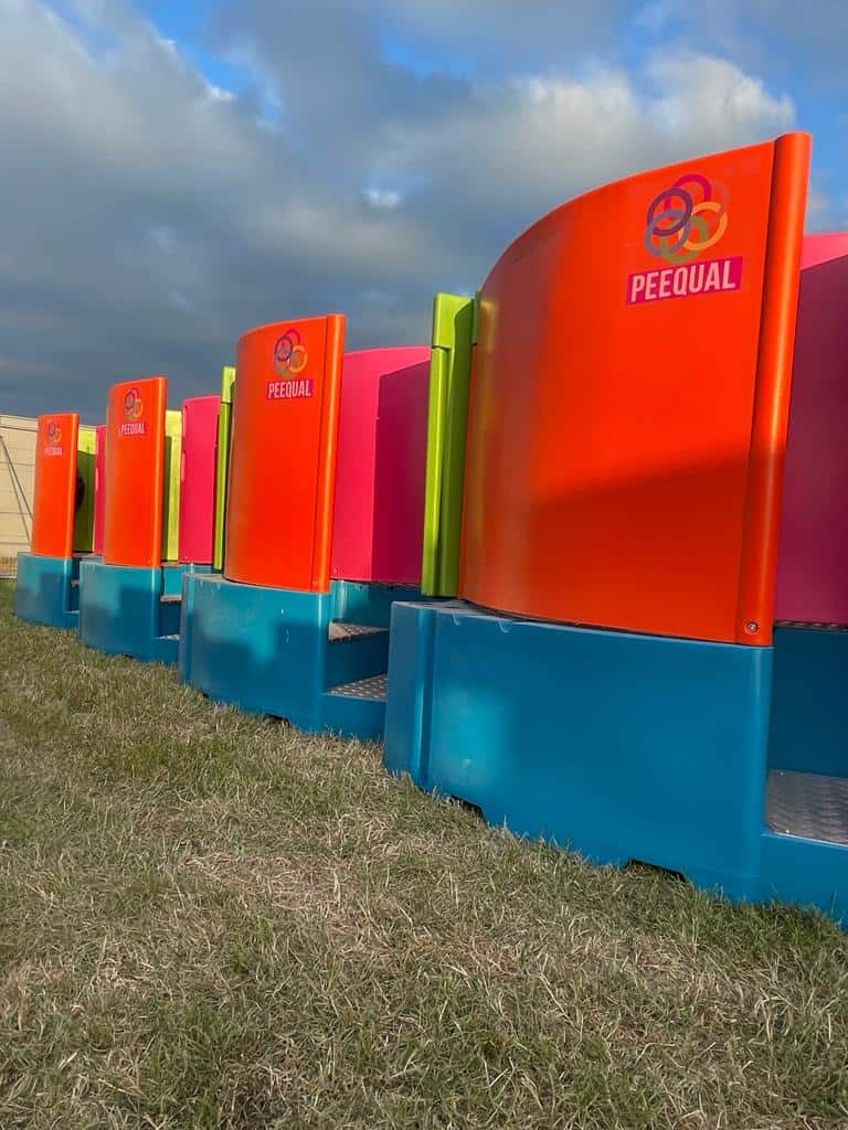 A row of Peequal urinals in vibrant orange, pink, green, and blue, showcasing their innovative design for outdoor events.