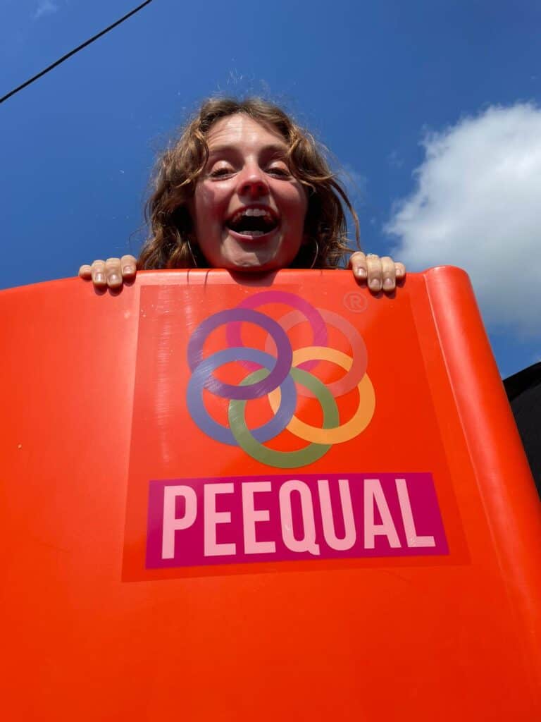 A woman peeking over the top of a Peequal urinal with the Peequal logo branded on the side.