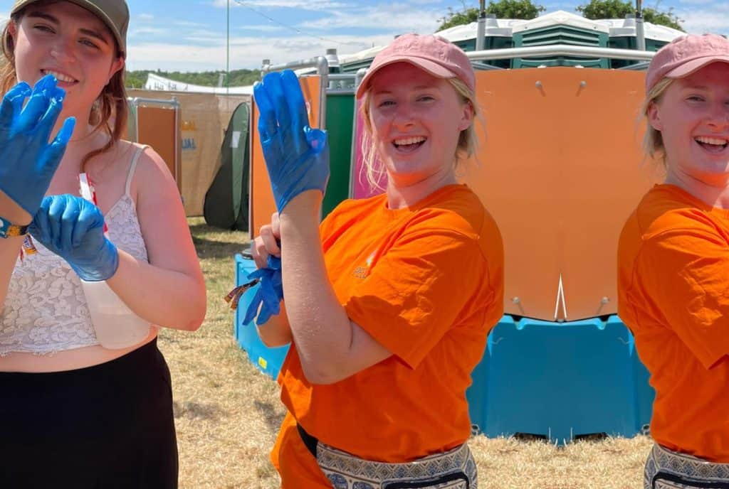 Two women wearing blue plastic gloves outside a set of Peequal urinals.