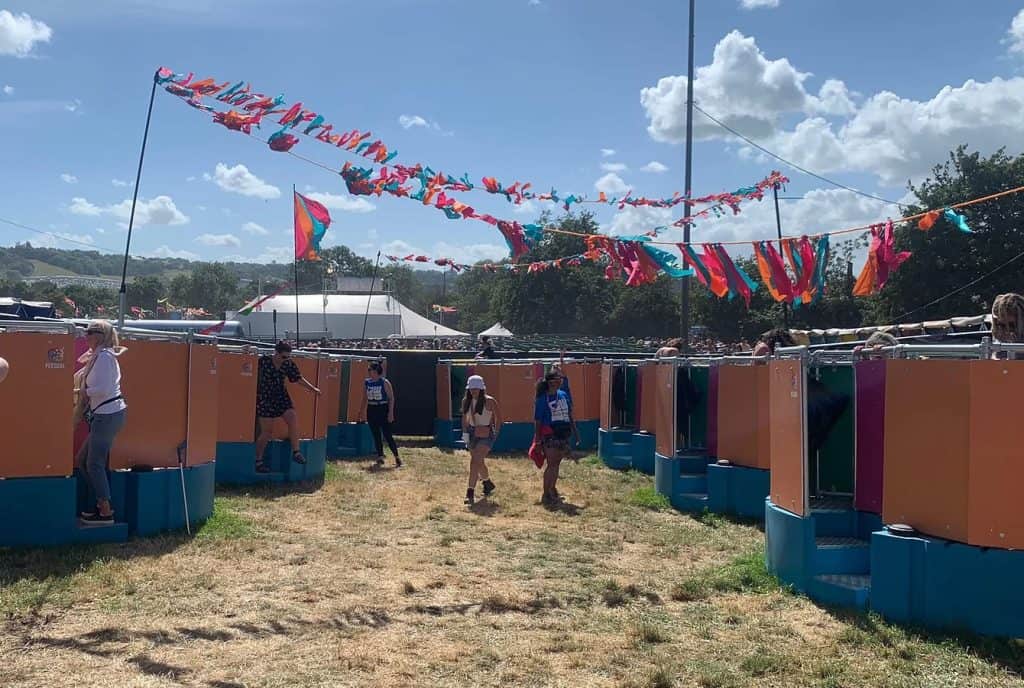 A row of Peequal urinals in vibrant orange, pink, green, and blue, showcasing their innovative design for outdoor events underneath colourful bunting.
