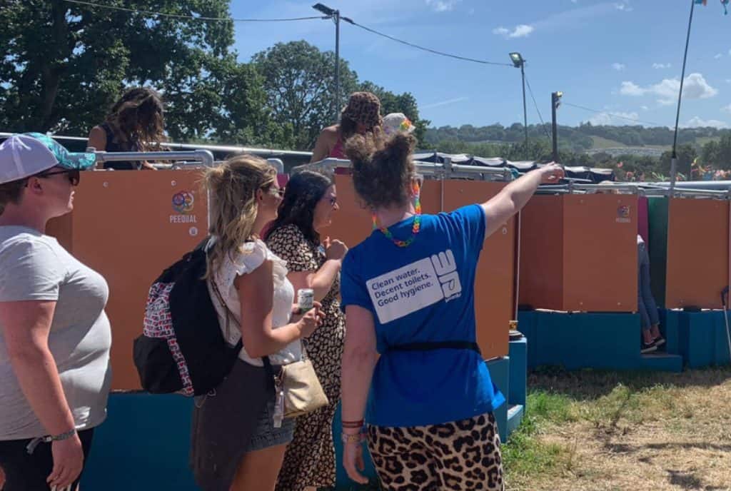 A volunteer in a blue t-shirt directs festival-goers to the Peequal urinals.