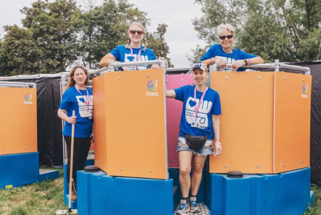 A group of four women in blue t-shirts standing around a Peequal urinal.